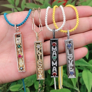 Handheld display of four colorful metal pendant necklaces with gemstones and letters