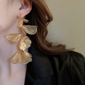 Detailed view of layered gold hollow flower tassel earrings on model with high texture
