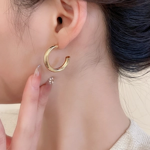 Gros plan d'une boucle d'oreille créole dorée en forme de C avec finition miroir polie