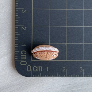 Miniature resin sandwich bread charm on a black measurement grid showing 2cm size