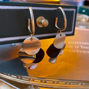 Detail von mehrlagigen Metall-Pailletten-Ohrhängern auf schwarzem Leder-Display