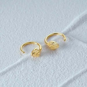 Macro shot of gold-plated snake hoop earrings with detailed serpent head on grey background