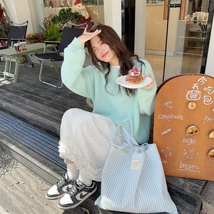 Green striped canvas tote bag paired with mint sweater and floral skirt in cafe setting