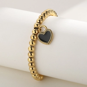 Vue détaillée d'un bracelet à billes dorées avec un pendentif cœur en émail noir