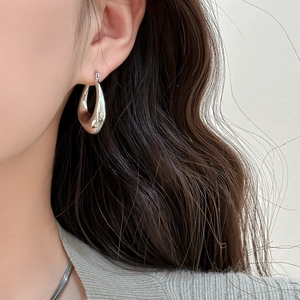 Minimalist silver oval drop earrings with polished metallic finish worn by model