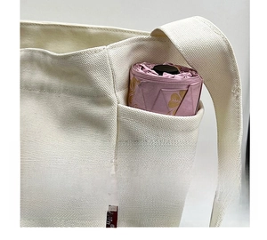 White canvas shoulder bag detail showing side pocket with a pink folding umbrella