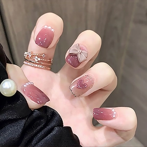 Détail de faux ongles dégradé rose avec papillon 3D, perles et cœur scintillant