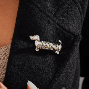 Detailed view of silver dachshund brooch with tricolor rope wrap on black wool coat lapel