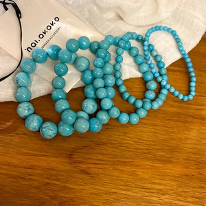 Detail of turquoise beaded elastic bracelets in various sizes on a wooden and linen surface