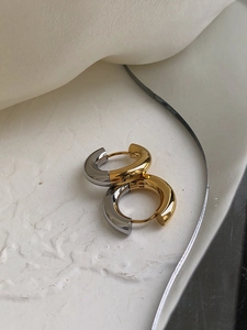 Macro detail of two-tone gold and silver stainless steel hoop earrings on textured white base