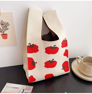Close-up of beige knitted tote bag with red apple patterns in a lifestyle setting