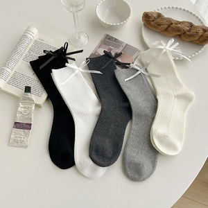 Flat lay of cotton crew socks with bows in five colors on a minimalist desk setting