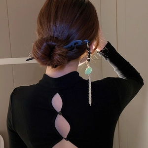 Detail of elegant wooden hair stick with green jade pendant and silver tassel on bun