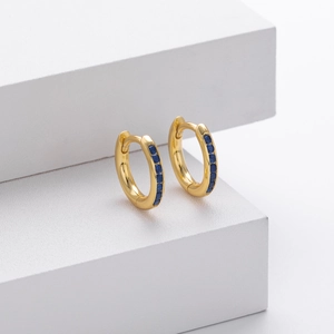 Close-up of gold hoop earrings featuring a row of inlaid blue zircons on a white stand