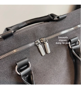 Detailed close-up of the smooth dual metal zippers on a dark gray canvas travel bag