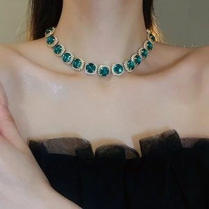 Luxurious gold necklace with emerald green round gemstones worn on a model's neck