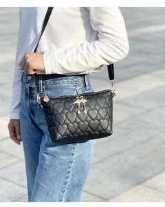 Detail of black crossbody bag with heart quilting and swan metal charm on model