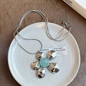 Macro detail of silver flower pendant with green resin stone and hammered metal texture