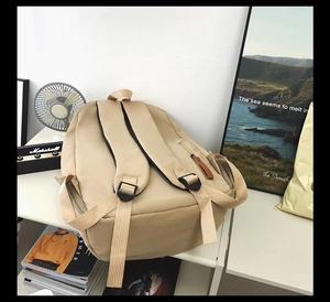 Detail view of thickened black padded shoulder straps on a beige nylon backpack