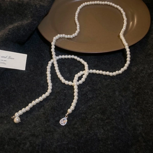 Detail of elegant pearl necklace with crystal water drop pendant on a dark plush surface
