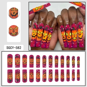 Faux ongles d'Halloween avec motifs de citrouilles orange et strass sur base magenta