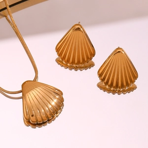 Dettaglio di collana con ciondolo a conchiglia dorata e orecchini su superficie a specchio
