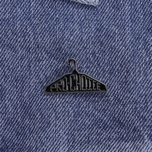 Minimalist Pro-Choice clothes hanger enamel pin on blue denim fabric background