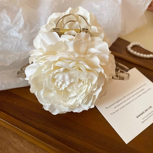 Top view of white floral shark hair clip on wooden tray with pearl necklace detail
