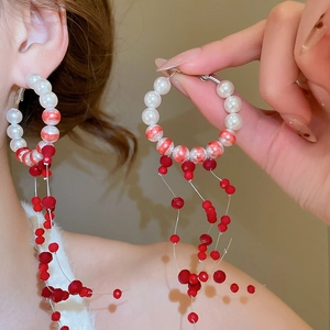 Detail of elegant hoop earrings with white pearls, red beads and metal tassels on model