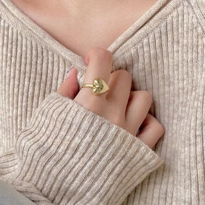 Detail of a polished gold heart-shaped 925 silver ring worn on a finger over a beige sweater