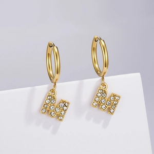 Detail of gold-plated M-letter earrings with sparkling zircon inlay on white stand