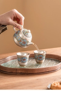 Macro shot of tea being poured from a cloisonné enamel teapot into matching cups