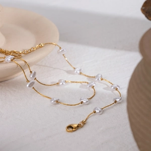 Detail of gold chain necklace featuring irregular white pearls on a ceramic tray
