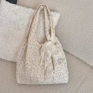 Floral canvas tote bag with white lace bow detail resting on a soft plush pillow