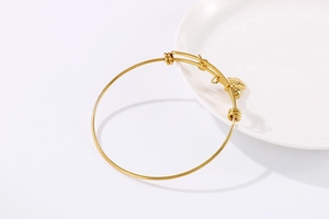 Detail of adjustable gold stainless steel bracelet with heart and ball charms on a white tray