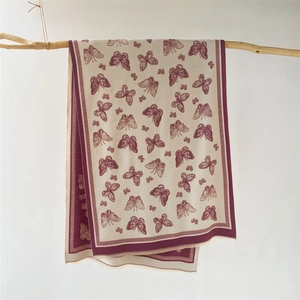 Detail shot of ivory cashmere shawl with purple butterfly prints and fringe hanging on wood