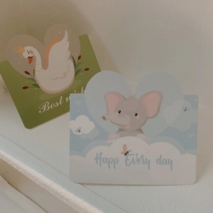 Close-up of cartoon style birthday cards with swan and elephant patterns and best wishes text
