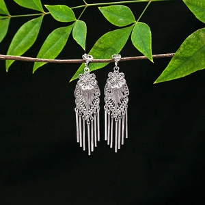 Ethnic silver tassel earrings with flower petals hanging on a natural green branch