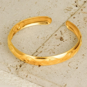 Detail of 18K gold plated evil eye cuff bangle with embossed texture on stone background