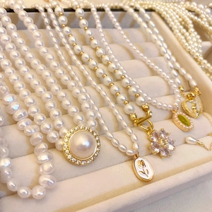 Détail de colliers en perles vintage avec pendentifs fleur et cœur dorés sur plateau