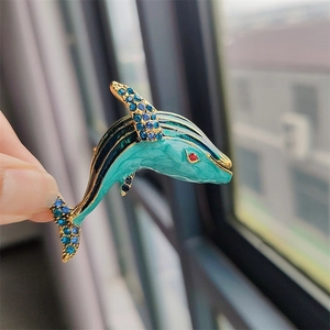 Macro detail of enamel dolphin brooch with blue rhinestones and gold metal finish