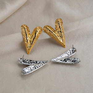 Detail of heart-shaped earrings with hammered texture in gold and silver finish