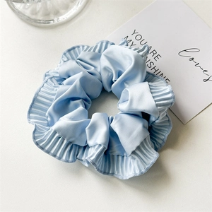 Close-up of light blue satin scrunchie featuring detailed pleated edges and silky texture