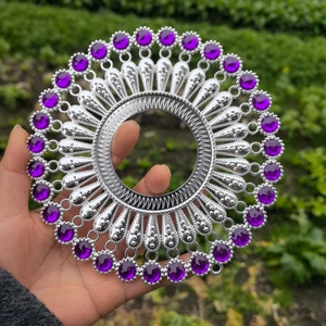Detailed view of silver metal wall decor with purple gems held in a garden setting