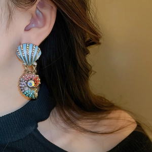 Detailed view of gold shell earrings with blue stripes and crystals on model