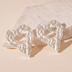 Detail of silver heart earrings with liquid metal texture on a textured stone surface
