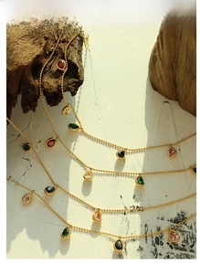 Detail shot of colorful teardrop zircon pendants on gold beaded necklaces with soft sunlight