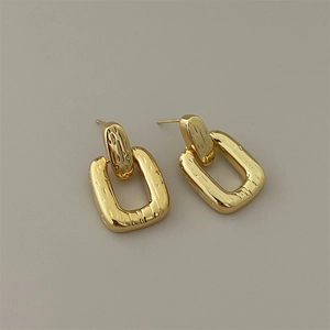 Detail shot of golden rectangular earrings with hammered metal texture for women