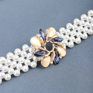 Detail of elegant pearl belt featuring a golden floral buckle with blue and cream gemstones