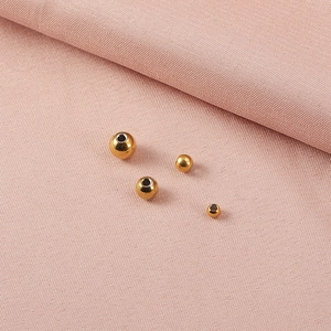 Macro shot of polished gold stainless steel spacer beads on pink textured fabric